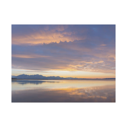 Calm lake at sunset with distant snow‑capped mountains and orange-pink skies reflected on water.