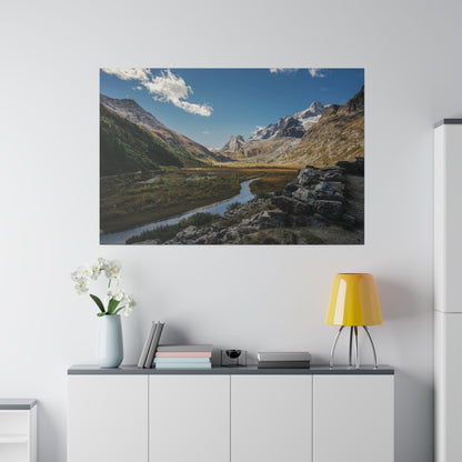 A mountain valley landscape with a winding river through green meadows, rocky slopes, and a blue sky.