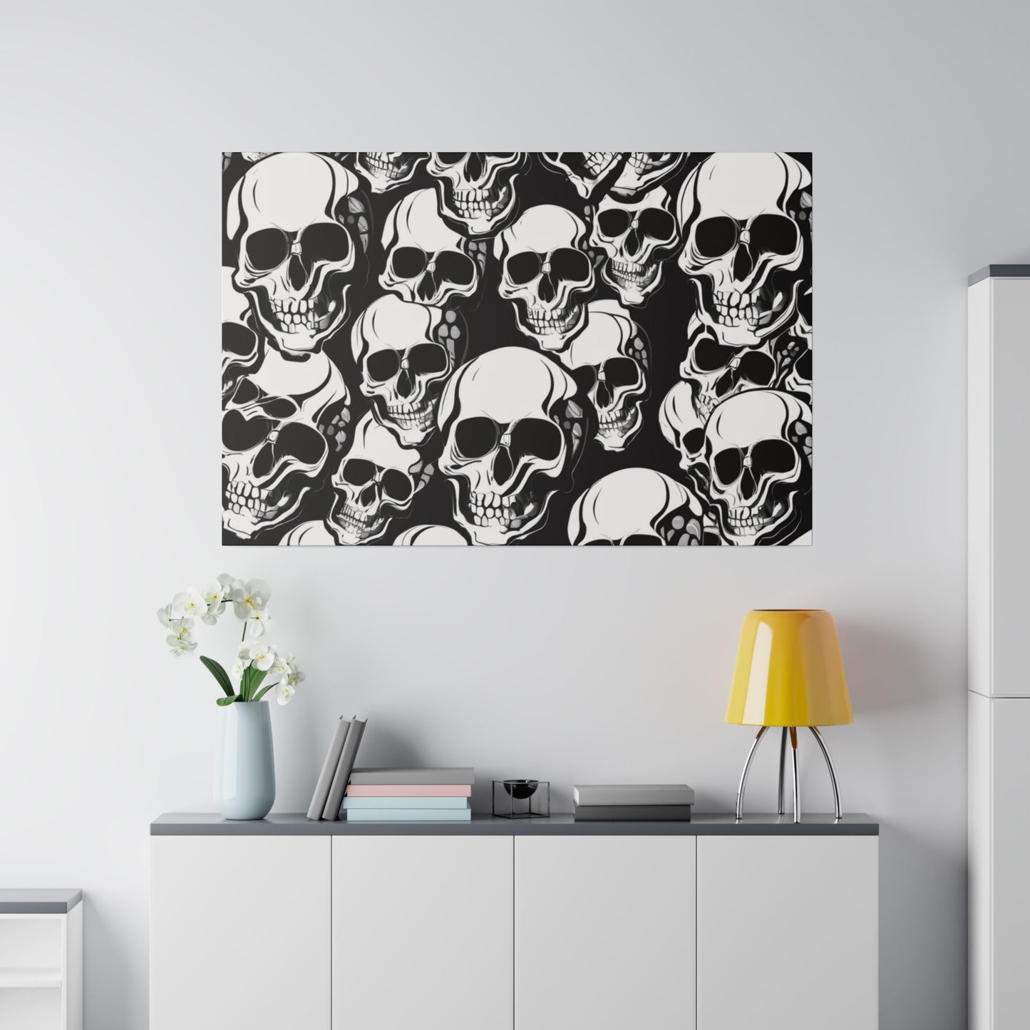 Poster with a dense pattern of white skulls on a black background hangs above a white cabinet with a yellow lamp.