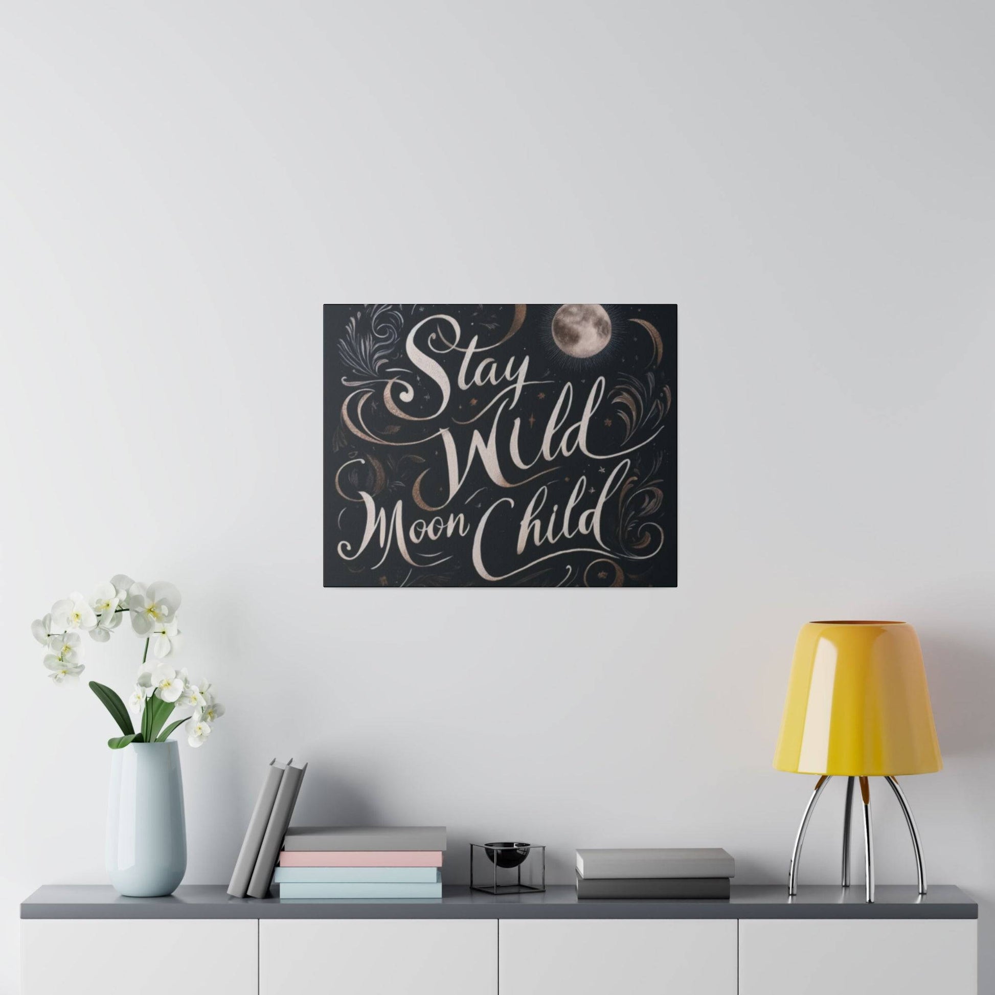 Black square wall art with white cursive text "Stay Wild Moon Child" and a small moon motif.