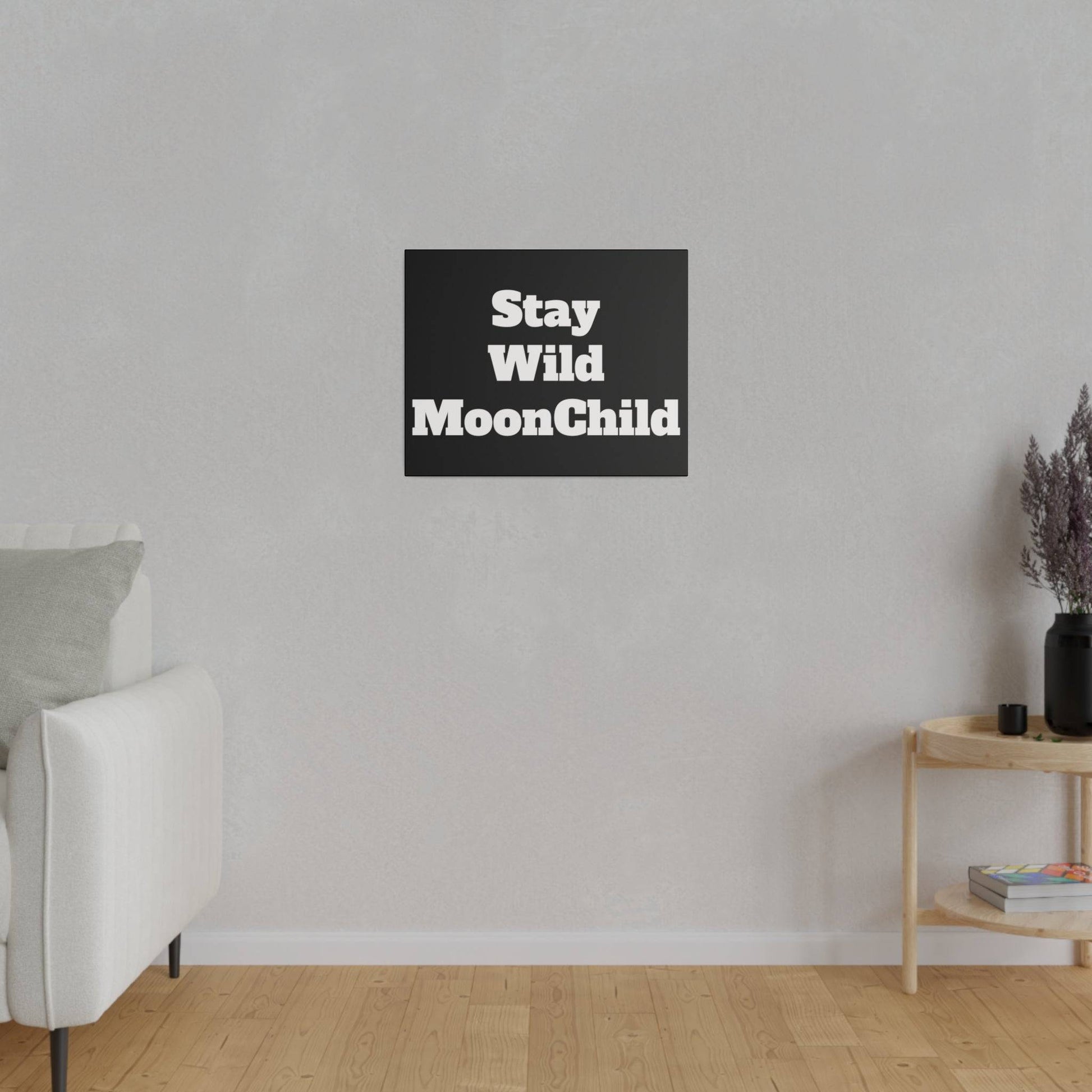 Gray textured living room wall with a black square wall art reading “Stay Wild MoonChild” above a light wood floor.
