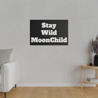 Black rectangular wall art with bold white text "Stay Wild MoonChild" mounted on a light gray living room wall.
