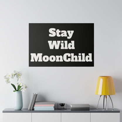 Black rectangular wall art reading 'Stay Wild MoonChild' in white typography, hung above a cabinet with a vase, books, and a yellow lamp.