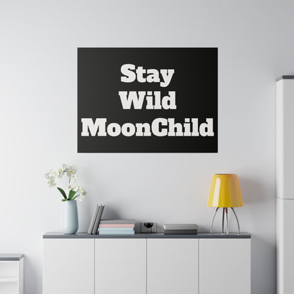Black square poster with bold white lettering Stay Wild MoonChild hanging above a white cabinet with a yellow lamp and flowers.