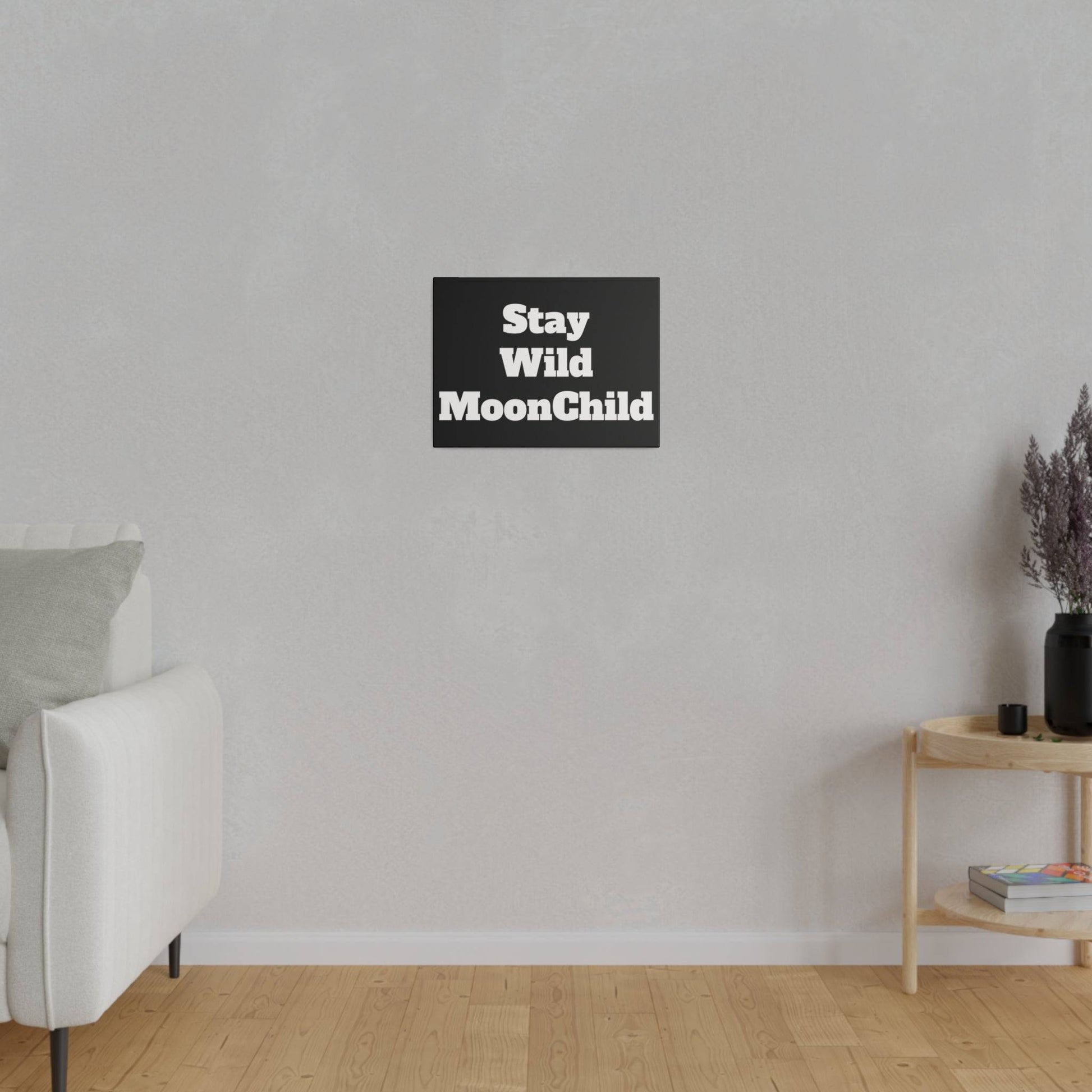 White sofa on the left in a minimal living room with a gray wall; a black square sign reading Stay Wild MoonChild hangs centered above.