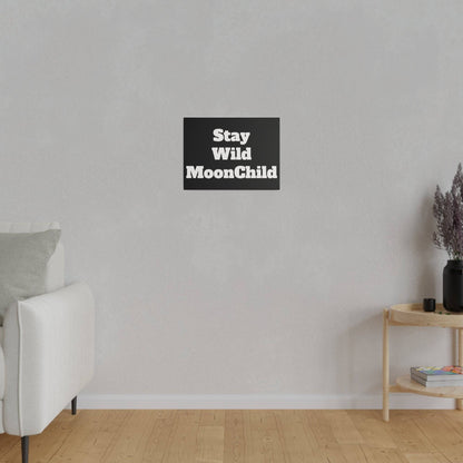 White sofa on the left in a minimal living room with a gray wall; a black square sign reading Stay Wild MoonChild hangs centered above.