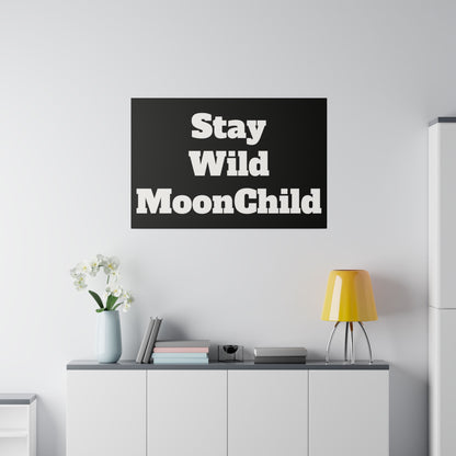Black poster with bold white text “Stay Wild MoonChild” hangs on a white wall above a white cabinet with a vase, books, and a yellow lamp.