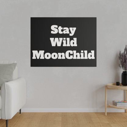 A gray living room wall with a black square wall art reading “Stay Wild MoonChild” in bold white letters above a light hardwood floor.