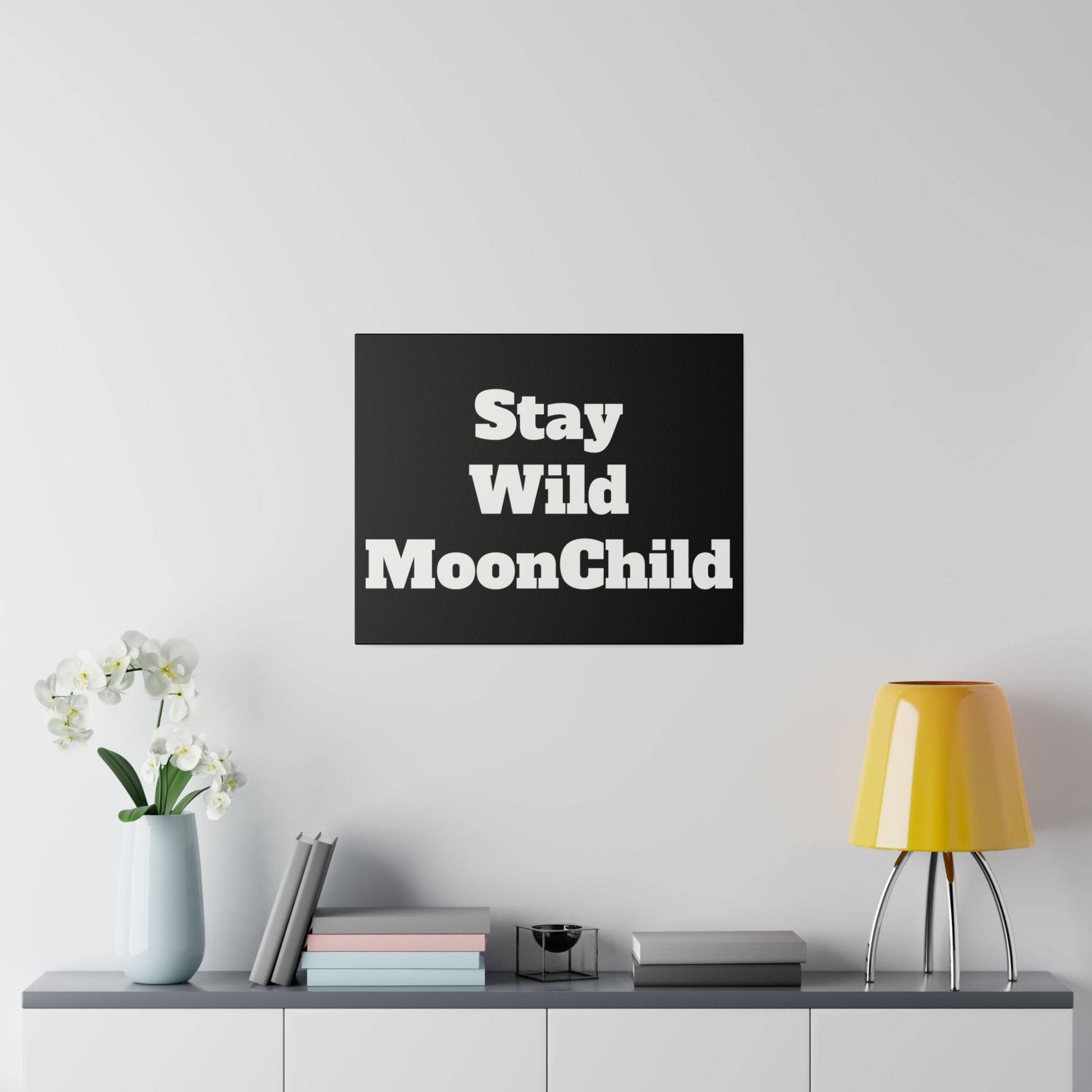 A black square wall print with bold white text reading "Stay Wild MoonChild" mounted above a gray console.