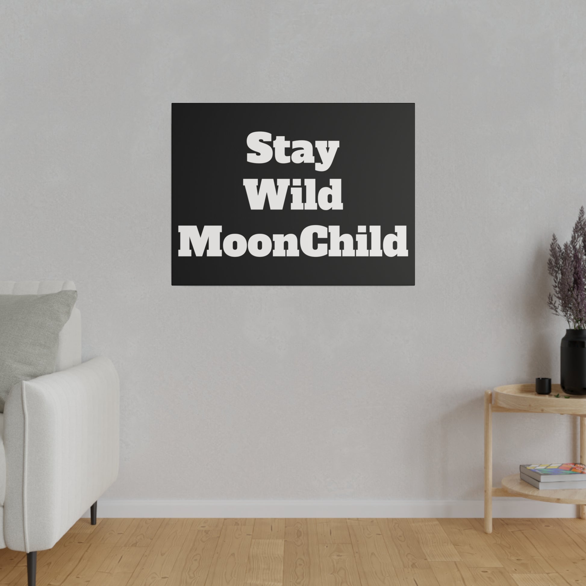 A black square wall art with the white text “Stay Wild MoonChild” hangs above a white sofa in a gray living room.