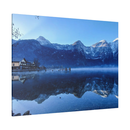 Calm alpine lake with snow-capped mountains, a wooden pier and small building on the shore, and blue reflections on the water.