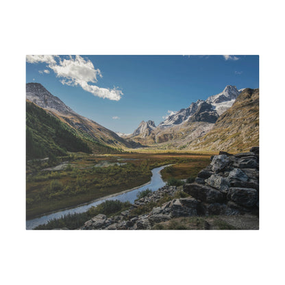 Rocky mountain valley with a winding river, green meadows, and snow-capped peaks under a blue sky.