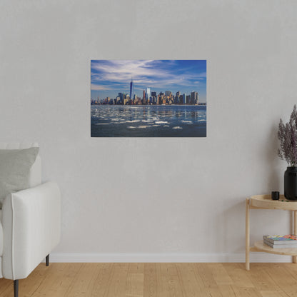 Photograph of the New York City skyline across a partly icy river, with blue sky and wispy clouds.