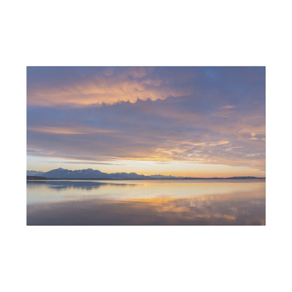 Calm lake at sunset with a purple-gold sky and distant snow-capped mountains, reflecting on the water.