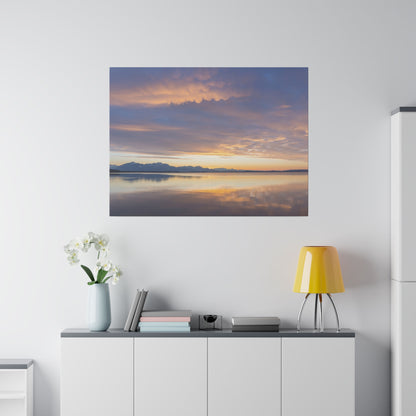 Framed photo of a sunset over a calm lake with distant mountains, reflecting orange and purple skies on the water.