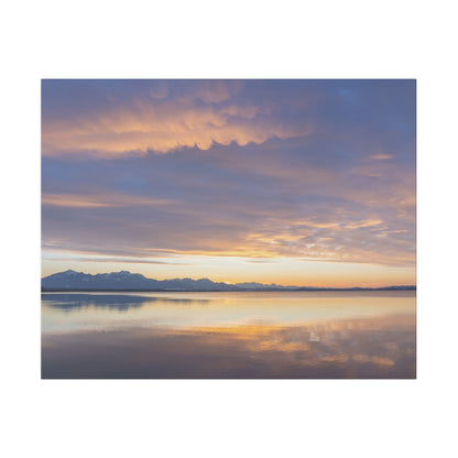 Calm lake at sunset with orange and purple sky, distant snow-capped mountains, and reflections on the water.