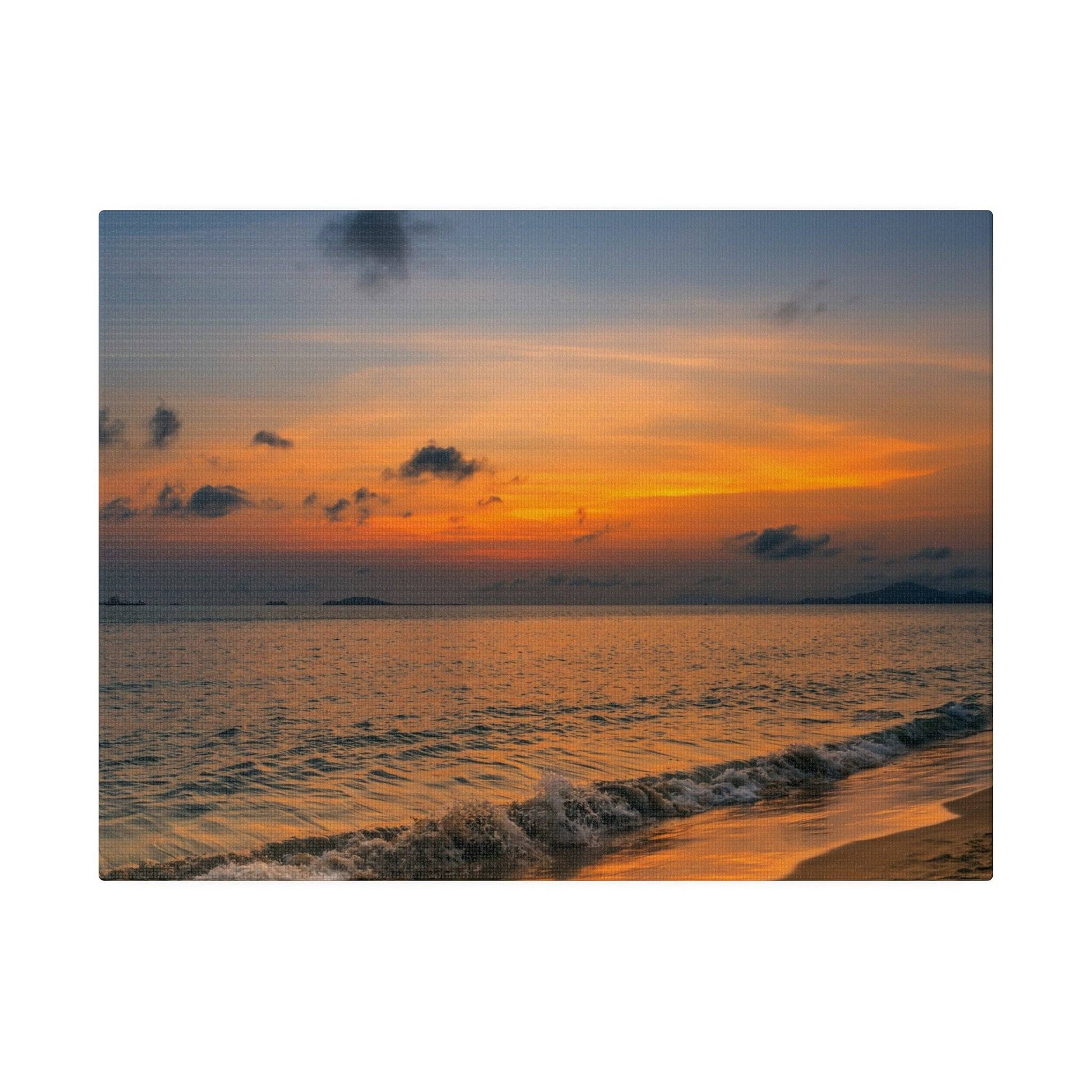 Sunset over calm sea with orange and blue sky, waves washing onto a sandy beach.