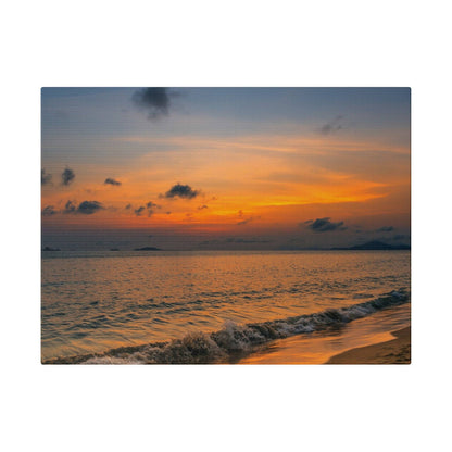 Sunset over calm sea with orange and blue sky, waves washing onto a sandy beach.