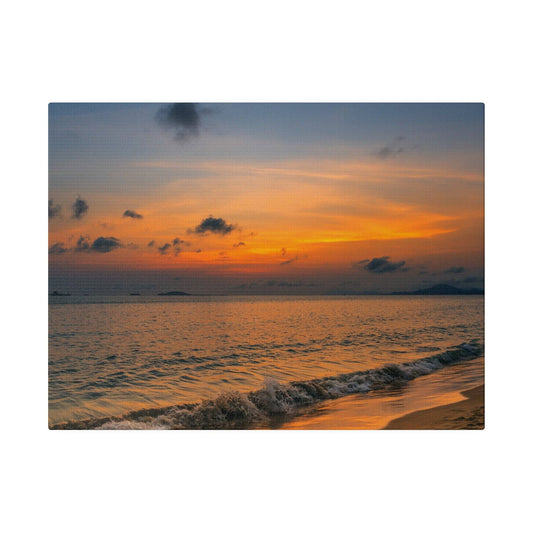 Sunset over calm sea with orange and blue sky, waves washing onto a sandy beach.