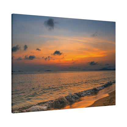 Beach scene at sunset: orange and blue sky over calm ocean with small waves washing onto the sandy shore.