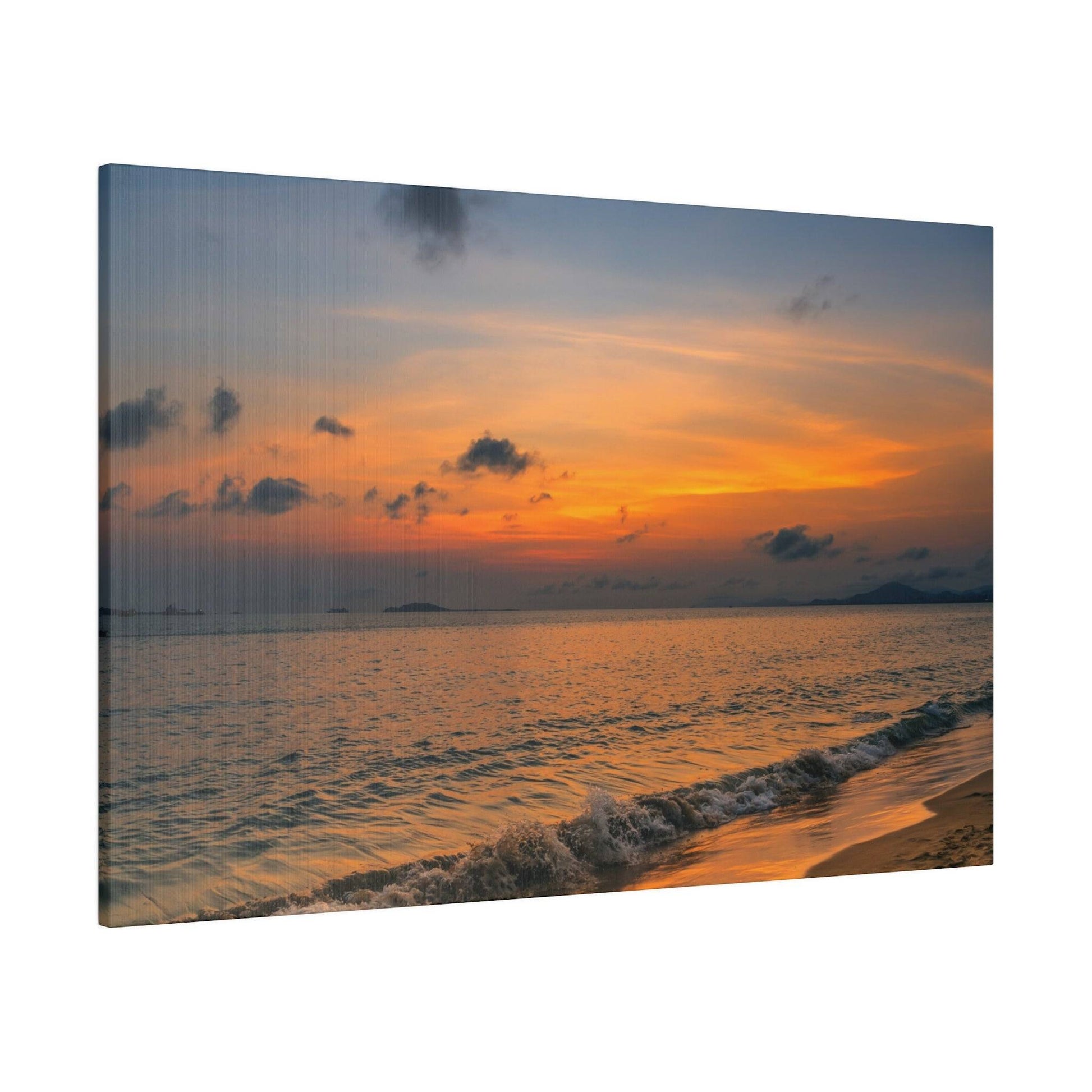 Sunset over the ocean with an orange and blue sky, small waves breaking on a sandy shoreline.