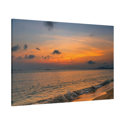 Sunset over the ocean with an orange and blue sky, small waves breaking on a sandy shoreline.