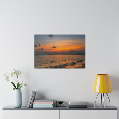 Photo print of a sunset over the ocean, with an orange sky, dark clouds, and waves washing onto a sandy beach.