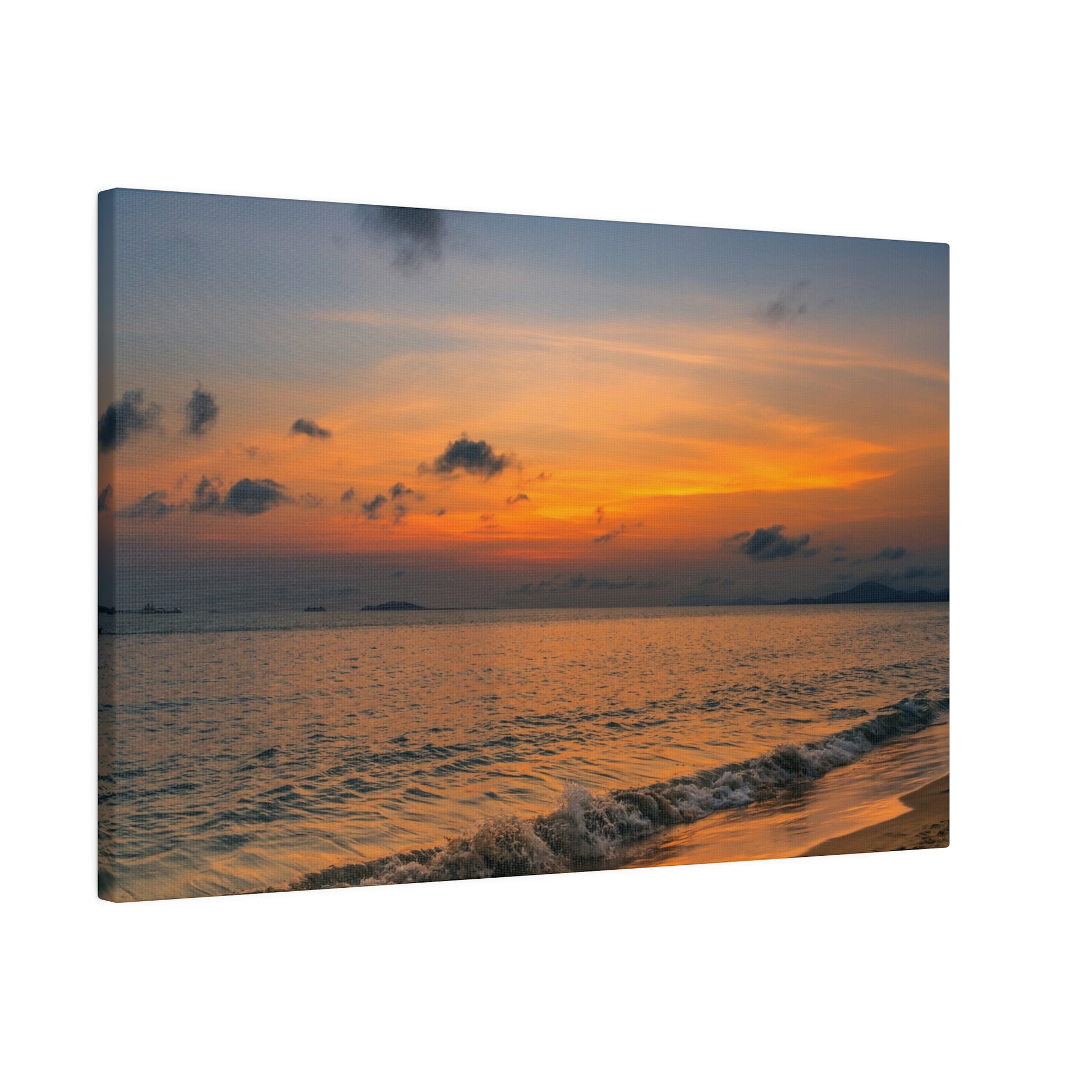 Photo of a calm ocean at sunset with an orange-yellow sky and small waves washing onto a sandy shore.