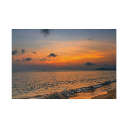 Sunset over a calm sea with orange sky, blue horizon, and gentle waves washing onto a sandy beach.