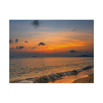Orange and blue sunset over calm sea, with gentle waves washing onto a sandy beach.