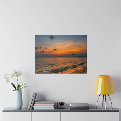 Square photo of a sunset over the ocean with orange and blue sky, mounted on a light wall above a console.