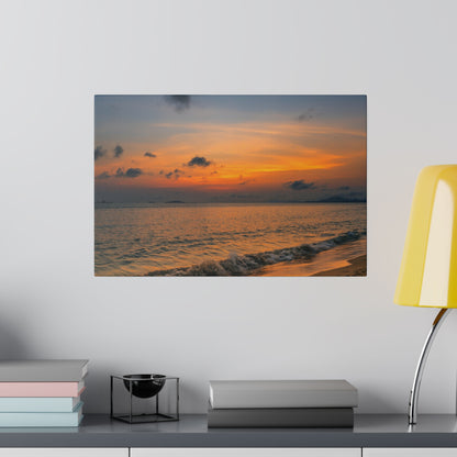 Framed photograph of a sunset over the ocean with an orange sky, gentle waves, and a sandy shoreline.