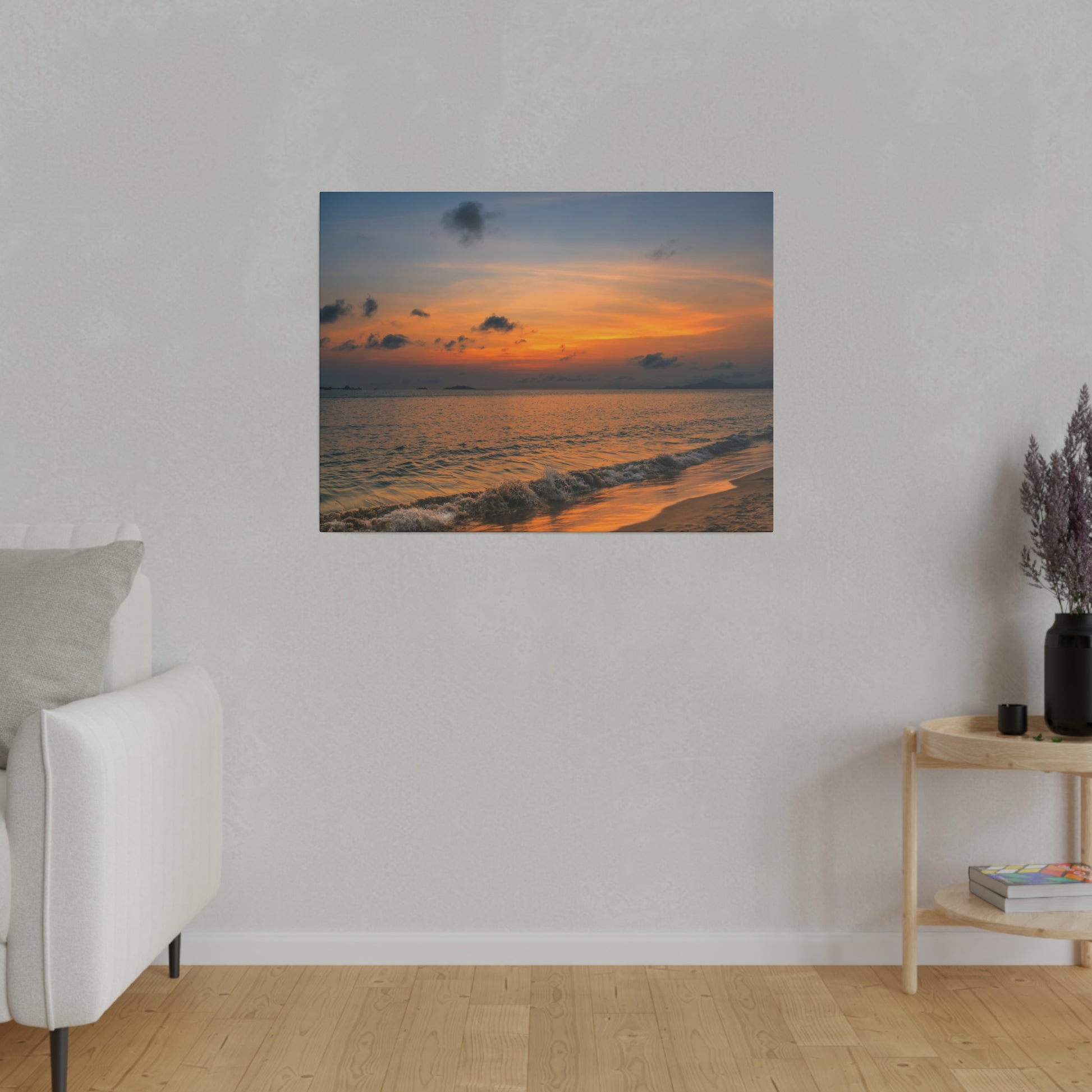 A wall-mounted canvas print of a sunset over the ocean with orange sky and gentle waves on a sandy shore.