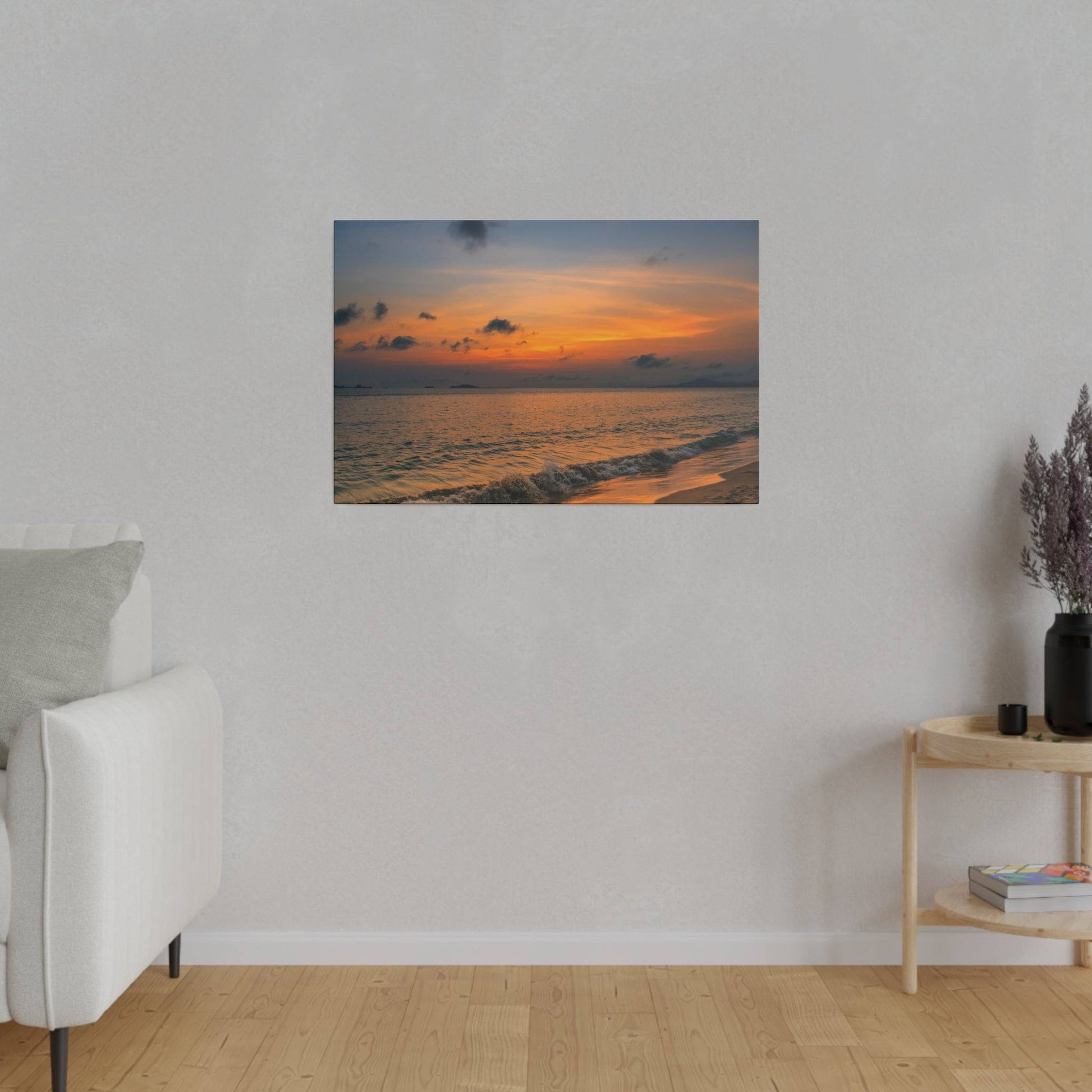 A framed seaside sunset print hangs on a light gray wall above a white sofa in a living room.