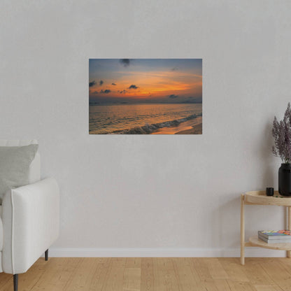 A framed seaside sunset print hangs on a light gray wall above a white sofa in a living room.