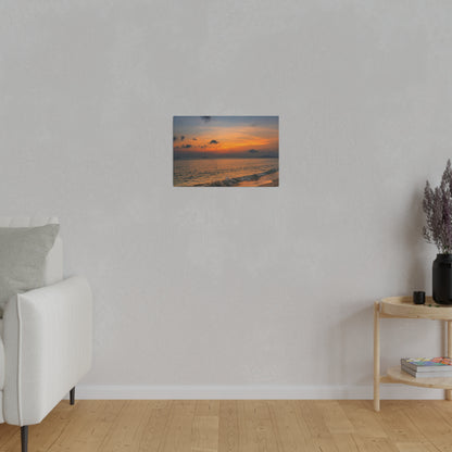 Small landscape painting of an orange sunset over the ocean mounted on a light gray wall in a minimalist living room.