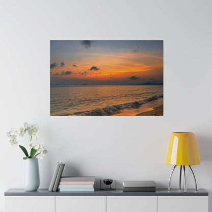 Photo of a sunset over the ocean with orange and blue sky, and gentle waves on a sandy beach.