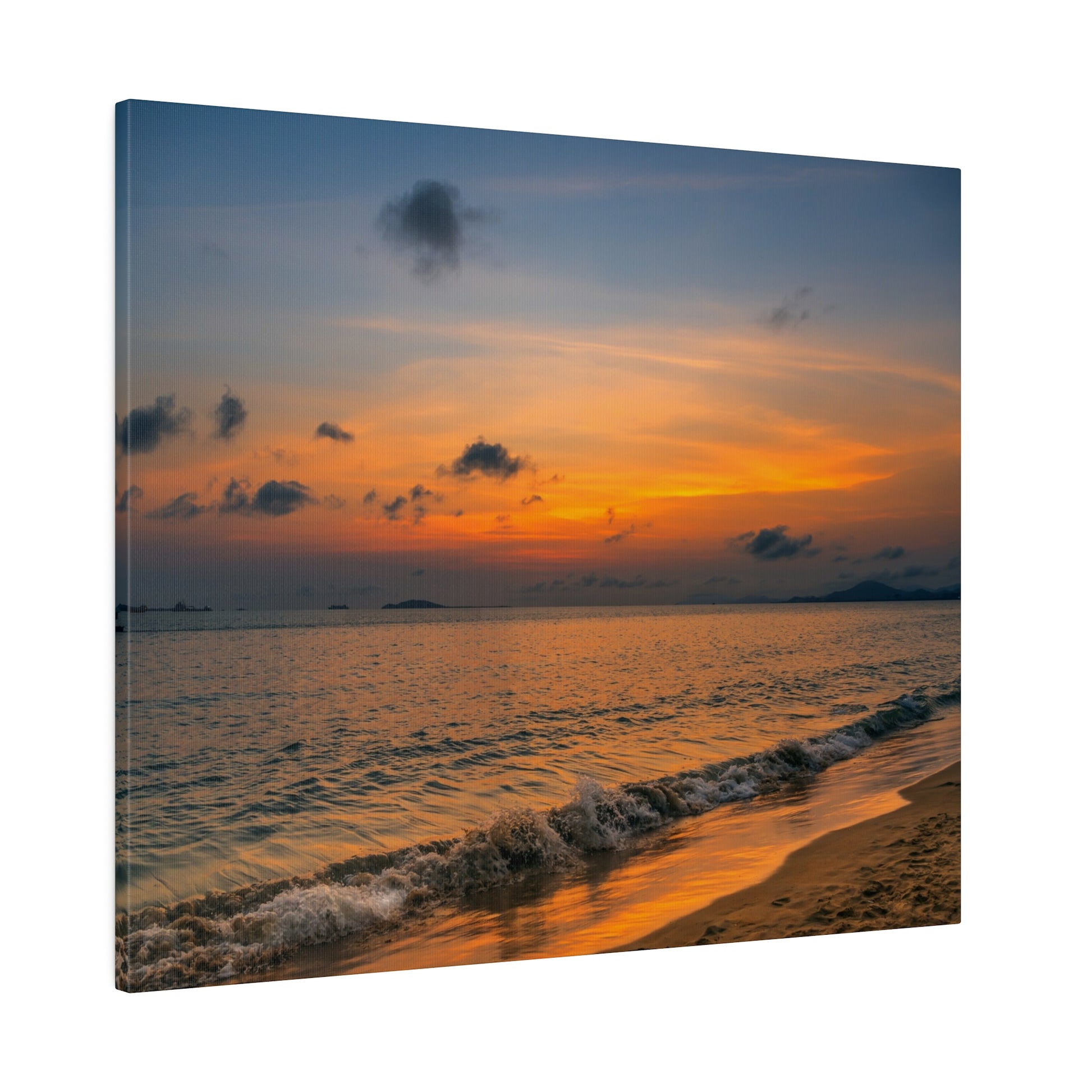 Sunset over the ocean with an orange sky, scattered clouds, and gentle waves washing onto a sandy shoreline.