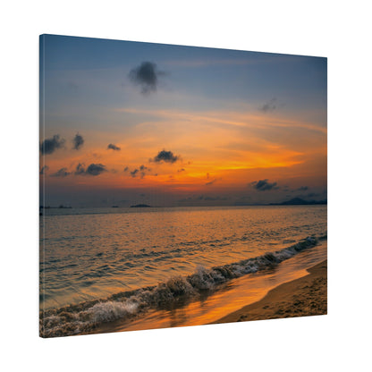 Sunset over the ocean with an orange sky, scattered clouds, and gentle waves washing onto a sandy shoreline.