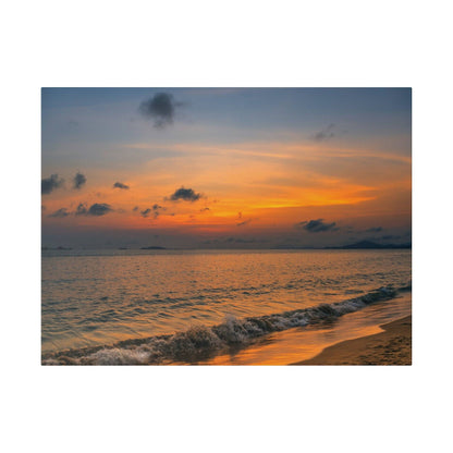 Sunset over calm sea with an orange sky, distant islands on the horizon, and gentle waves washing onto the sandy shore.