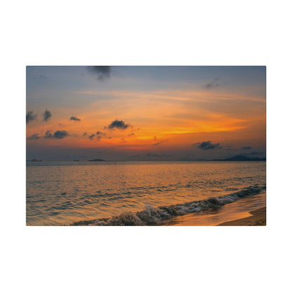 Sunset over a calm ocean with an orange-pink sky and waves washing onto a sandy beach.