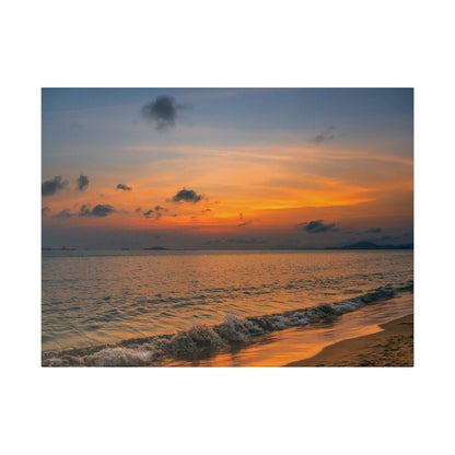 Sunset over a calm ocean with orange and blue sky, waves lapping a sandy beach.