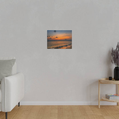 Small square wall art depicting a sunset over the ocean, mounted on a light gray wall above a white sofa in a living room.