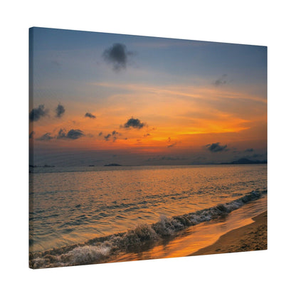 A sunset over the ocean with an orange and pink sky, distant islands, and gentle waves washing onto a sandy shore.