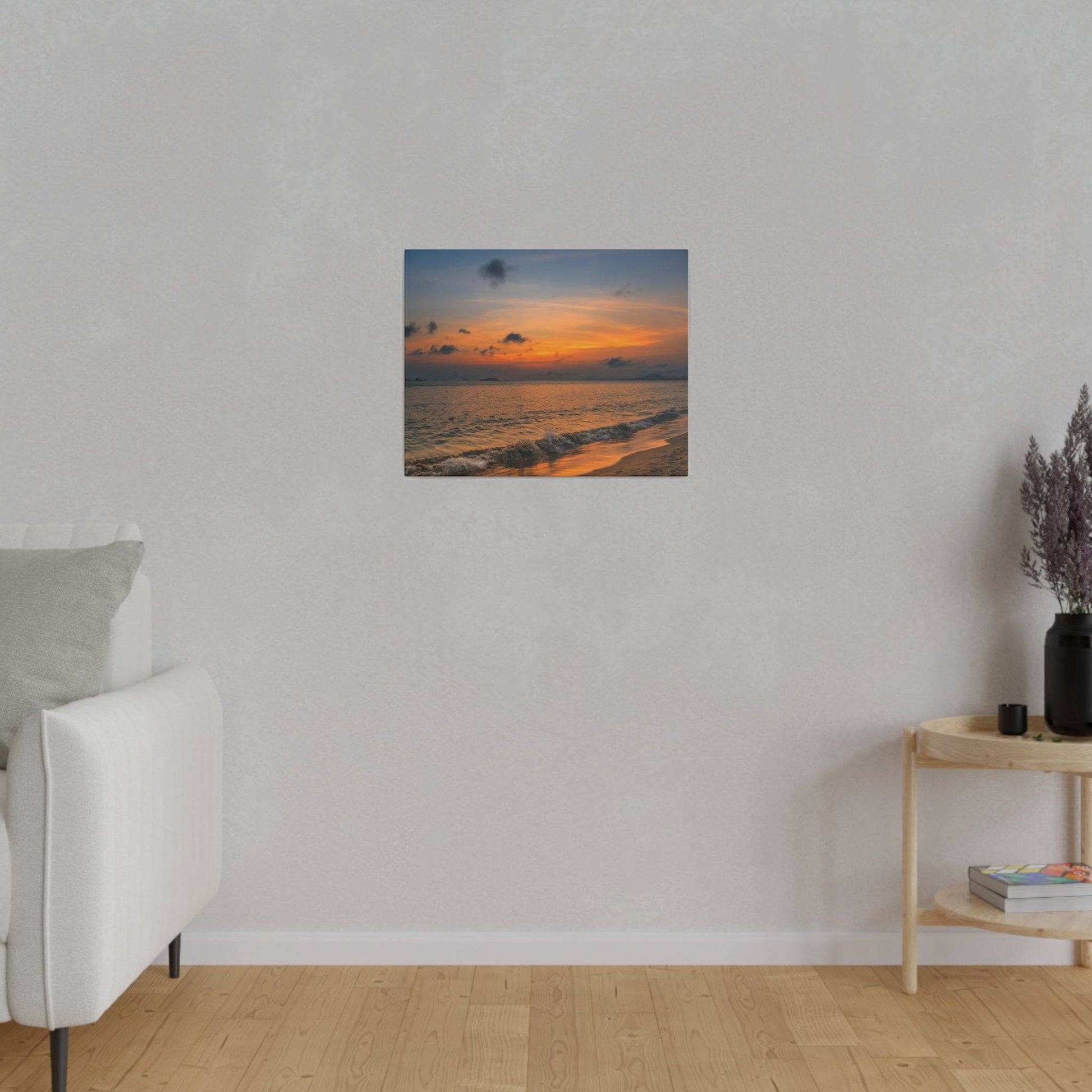 Small square painting of a sunset on a beach hangs on a light gray wall above a white sofa.