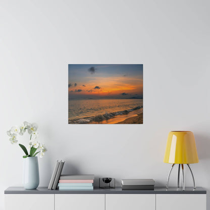 Square photo of a sunset over the ocean with orange and blue skies and gentle waves on a sandy shore.