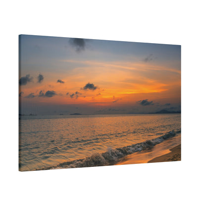Photo of a sunset over the ocean with orange clouds, calm water, and a sandy shoreline.