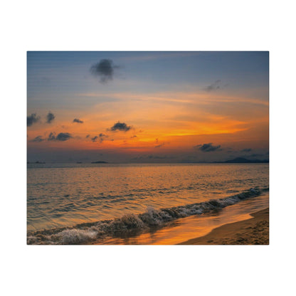 Orange and blue sunset over calm sea with gentle waves washing onto a sandy beach.