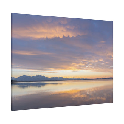 Sunset over a calm lake with orange and purple skies, snow-capped mountains reflected on the water.