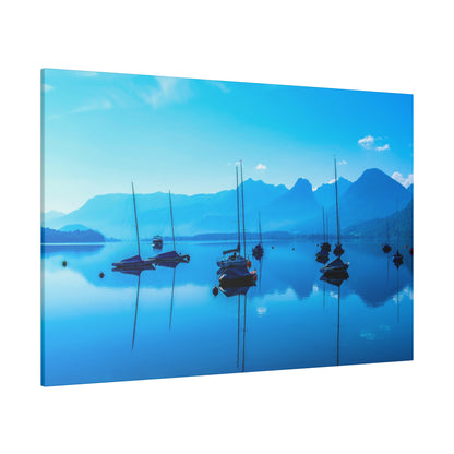 Calm blue lake with several sailboats anchored, mountains in the background under a clear blue sky.